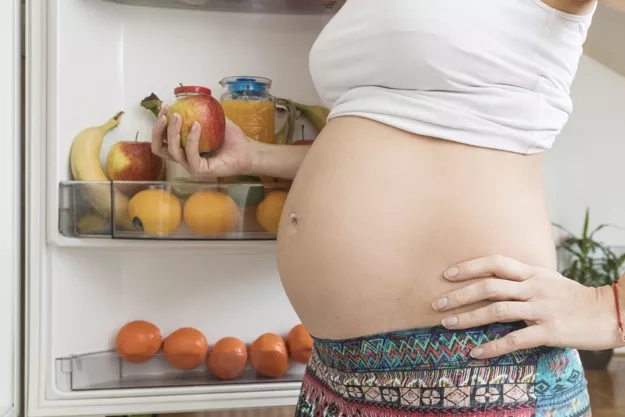 A pregnant lady holding an apple in her hand.